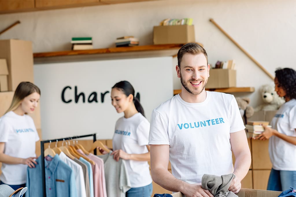 Group of people sorting clothing indoors – smiling man in foreground holding folded garment.