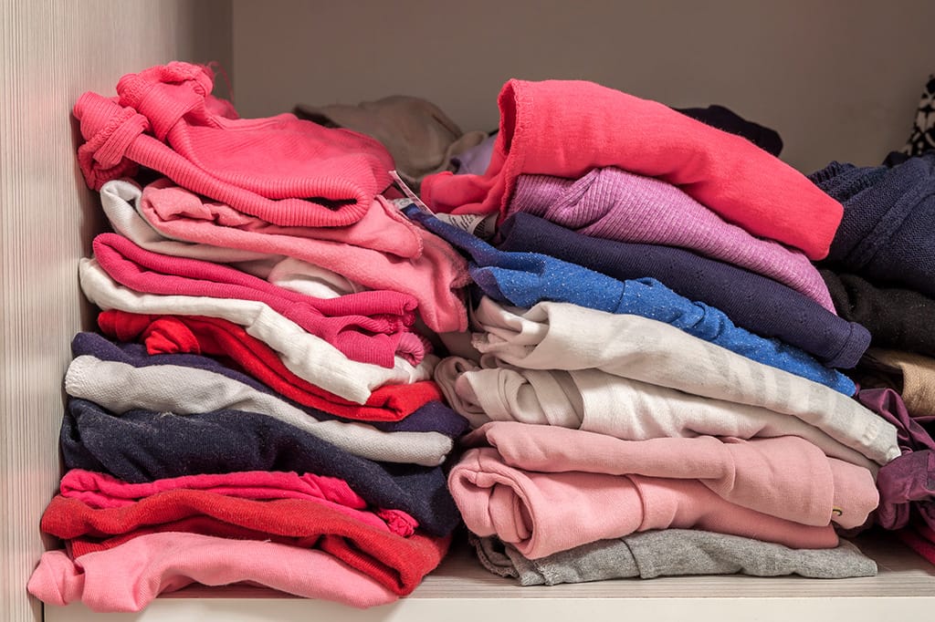 Neatly stacked piles of folded clothes in shades of red, pink, blue, and white.