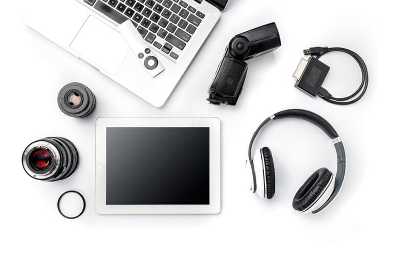 Assorted electronics including a laptop, tablet, camera lenses, headphones, and cables on a white background.