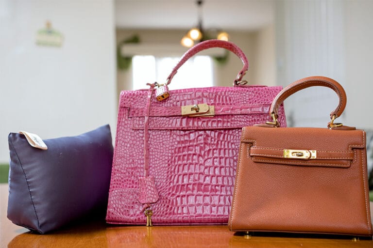 Three handbags, including a large pink crocodile leather bag and a smaller brown leather bag, displayed indoors.